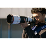 Photographer using a professional camera with a large telephoto lens outdoors.