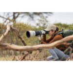 Photographer using a professional camera with a telephoto lens outdoors.
