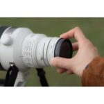 Person adjusting a telephoto lens on a professional camera outdoors.