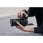Person holding a Sony mirrorless camera with a zoom lens, showcasing photography gear.