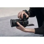 Person holding a Sony mirrorless camera with a zoom lens, showcasing photography gear.