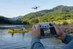 Person controlling DJI Mini 3 drone with screen controller over river landscape.